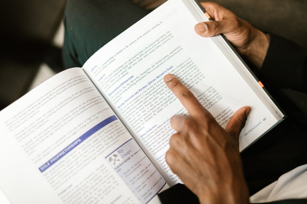 An adult reading a book on taxes, focusing on specific text with a pointing finger.