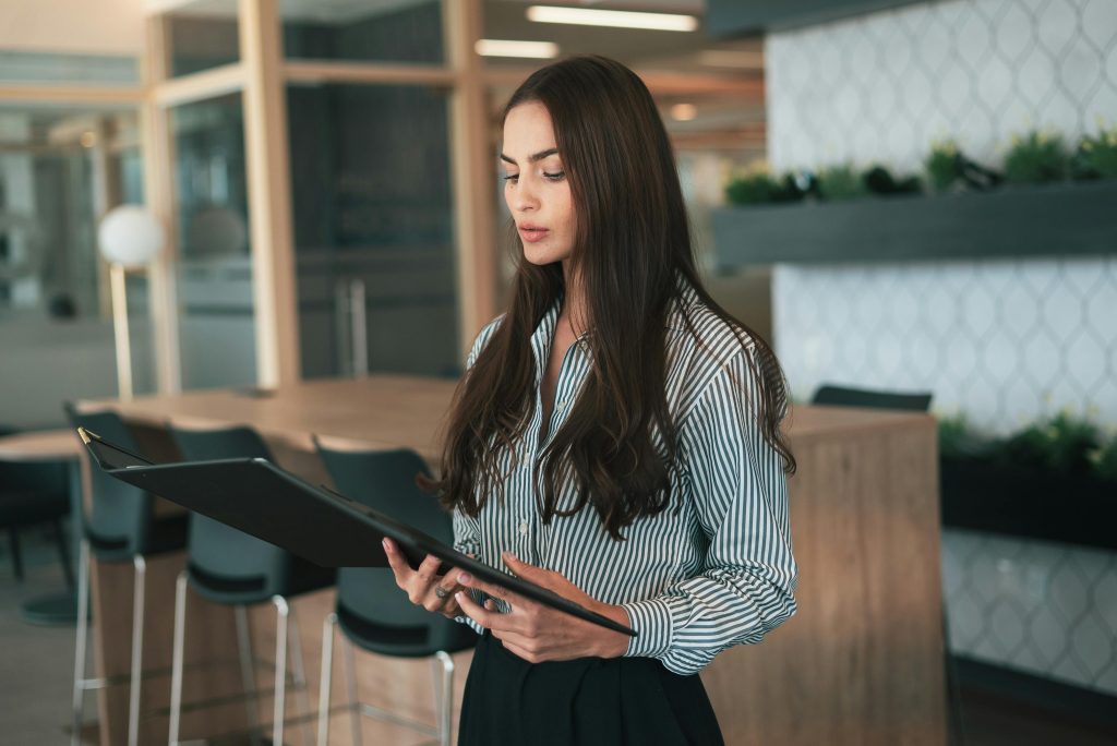 Focused businesswoman reviews documents in a modern office setting, showcasing corporate professionalism.