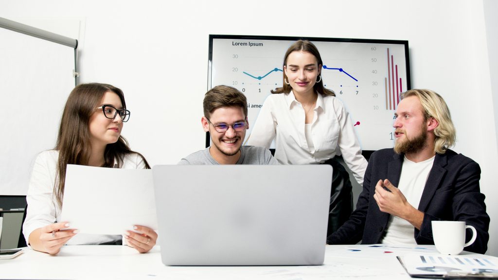 A group of young professionals collaborating in an office meeting, discussing ideas with a laptop and charts.